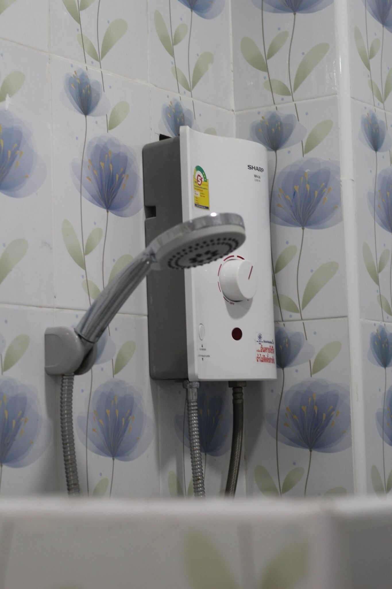 Casa de banho com chuveiro fixo na parede, revestida com azulejos estampados com flores.