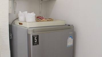 Un refrigerador compacto de acero inoxidable con un compartimento congelador, un estante pequeño encima y una tetera en la pared.