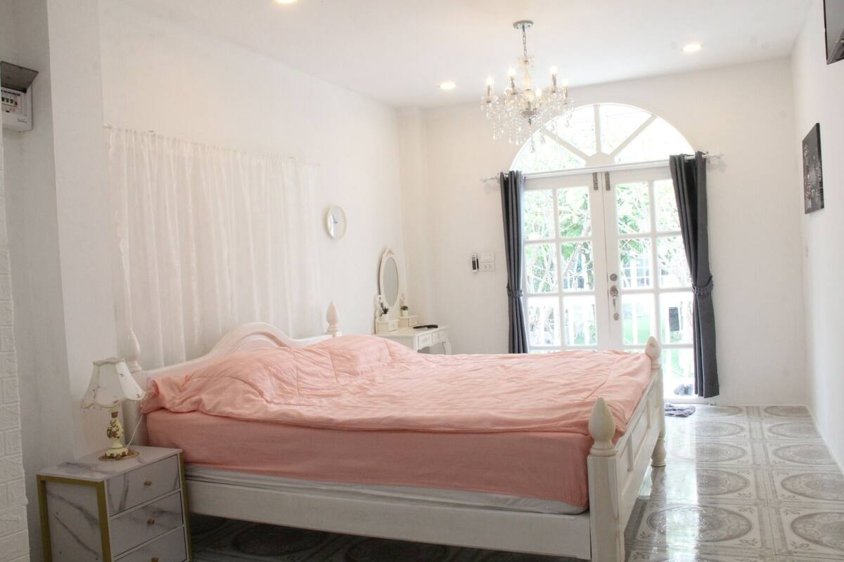 Une chambre à coucher comprenant un lit, une table de chevet, une commode et une fenêtre avec des rideaux.