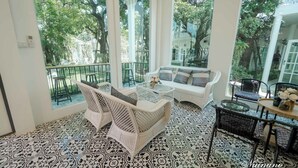 A room with a patterned floor, white furniture, and large windows offering a view of trees. - Bananaleaf Wedding Cafe & Resort (Nakhon Chai Si)