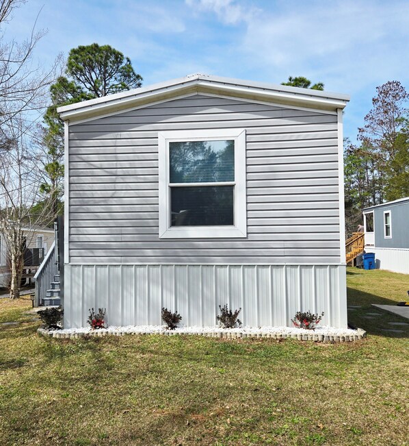 Une maison mobile de plain-pied, dotée d’une fenêtre centrale, d’un petit porche et d’une cour gazonnée.