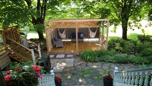 A covered outdoor seating area with a wooden deck, cushioned seating, and string lights. - Auberge Comme au premier jour (Saint-Pacôme)
