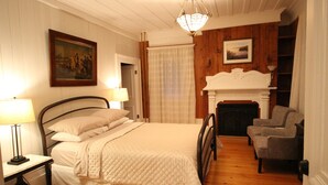A bedroom with a bed, bedside lamps, a fireplace, and a chair. - Auberge Comme au premier jour (Saint-Pacôme)
