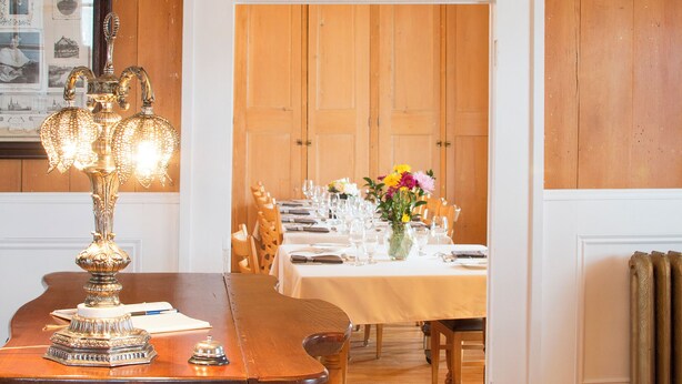A wooden-paneled room with a dining table set for a meal, a vintage lamp, and a framed picture on the wall. - Auberge Comme au premier jour (Saint-Pacôme)