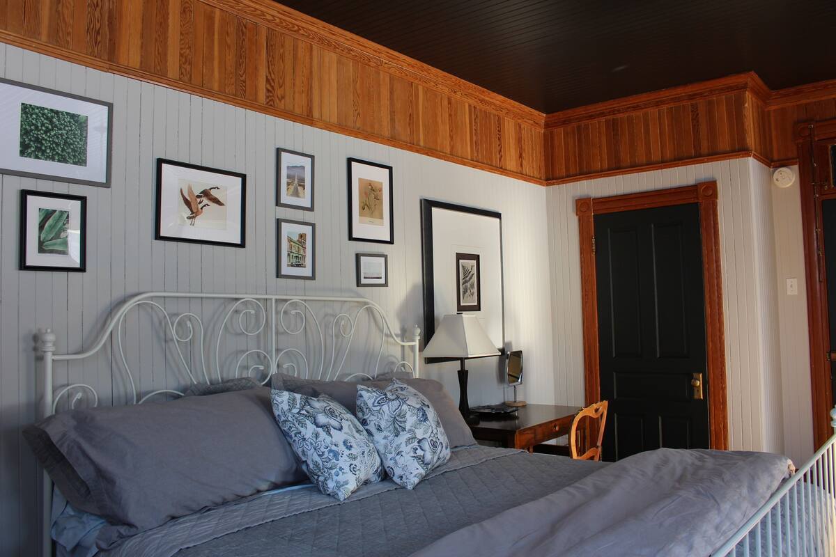 A bedroom with a bed, pillows, a nightstand, a lamp, and framed pictures on the wall.