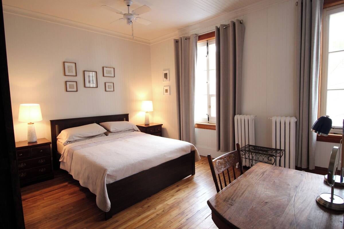 A bedroom with a bed, bedside lamps, a wooden table, and a chair.