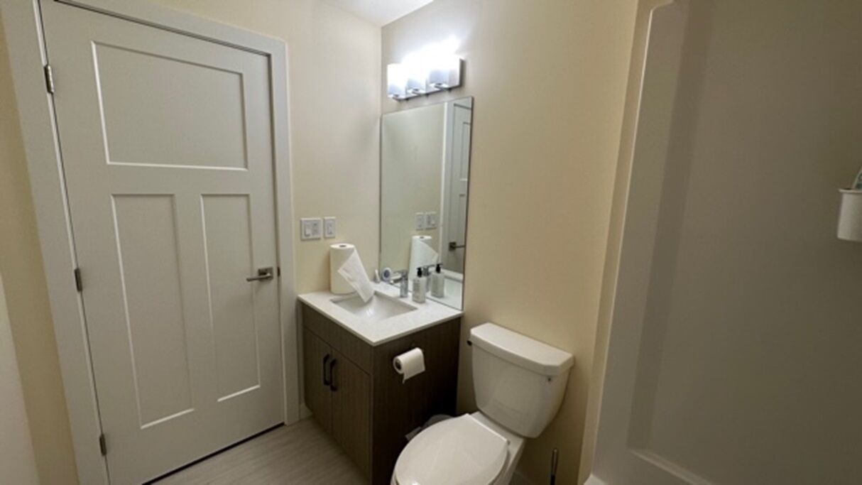 A small bathroom with a toilet, sink, mirror, and a door.