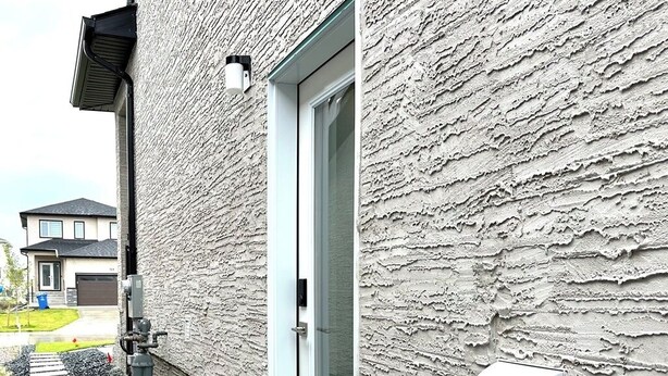 A building exterior with a textured facade, a door, and a mailbox. - Private Cozy 1 Bedroom Basement Suite (Winnipeg)