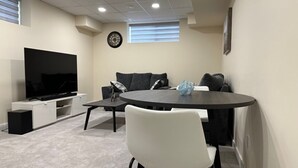 A modern living room with a flat-screen TV, a round dining table, and a sofa. - Private Cozy 1 Bedroom Basement Suite (Winnipeg)