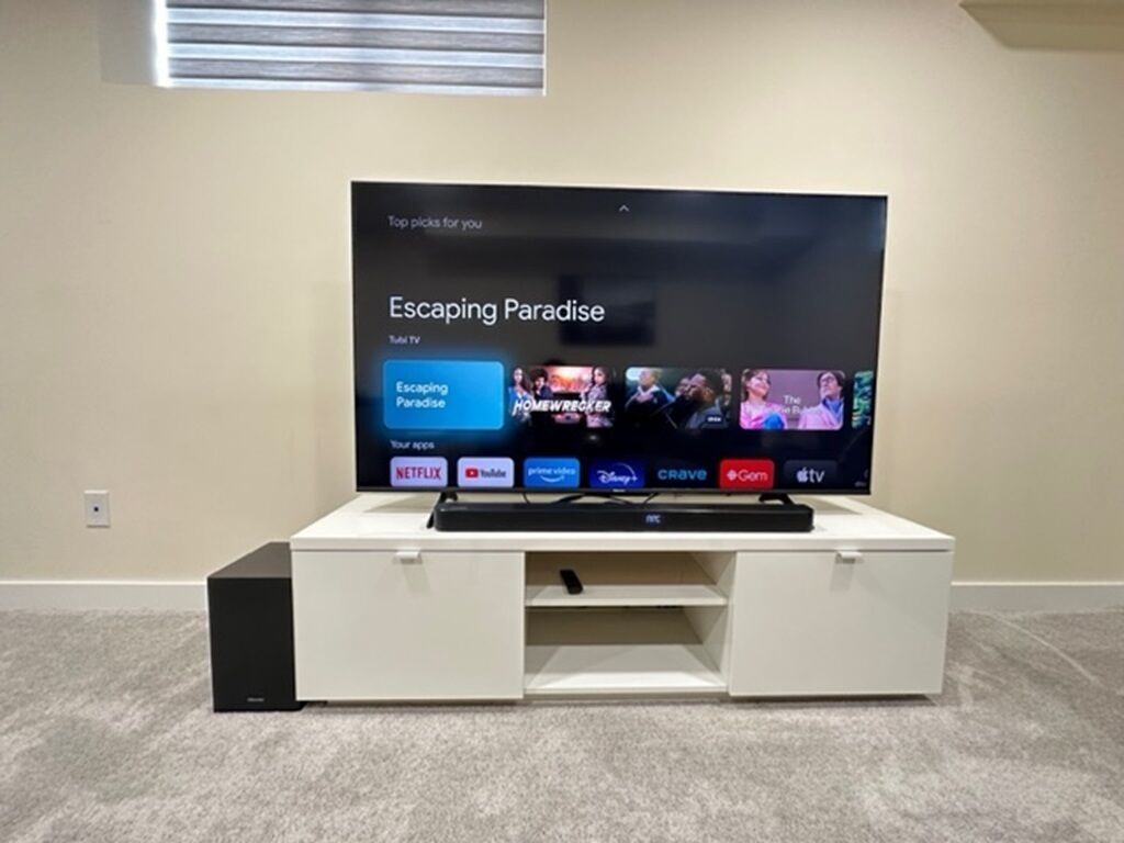Televisão de tela plana em um móvel branco com controle remoto.