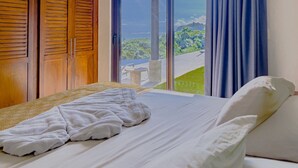 A bedroom with a bed, a wooden wardrobe, and a view of a green landscape through large windows. - Luxury Home With Ocean View (Provincia de Guanacaste)