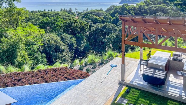 A pool area with a pergola and outdoor seating, surrounded by lush greenery and a view of the ocean. - Luxury Home With Ocean View (Provincia de Guanacaste)