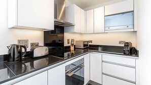 A modern kitchen with white cabinets, a black countertop, a stainless steel range hood, a toaster, and a kettle.