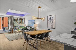 Una sala de estar moderna con comedor, cocina con encimeras de mármol y un amplio ventanal con cortinas.