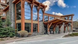 A modern building with large windows, a stone facade, and a wooden entrance canopy. - Exquisite condo, Mountain Views (Canmore)