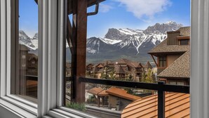 A mountain view from a window with wooden balconies, a mountain range, and residential buildings. - Exquisite condo, Mountain Views (Canmore)