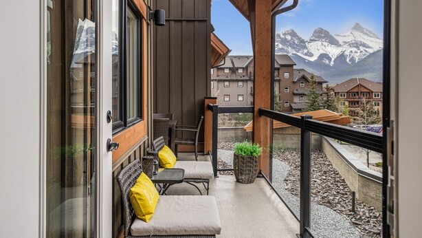 A balcony with a sofa, chairs, and a small table, overlooking a mountain view. - Exquisite condo, Mountain Views (Canmore)