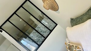 A room with a large window, a woven wall decoration, and a bed with patterned pillows. - Constance de Bretagne  (Batz-sur-Mer)