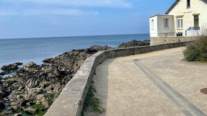 A coastal building with a stone wall and a paved path leading to the sea. - Constance de Bretagne  (Batz-sur-Mer)