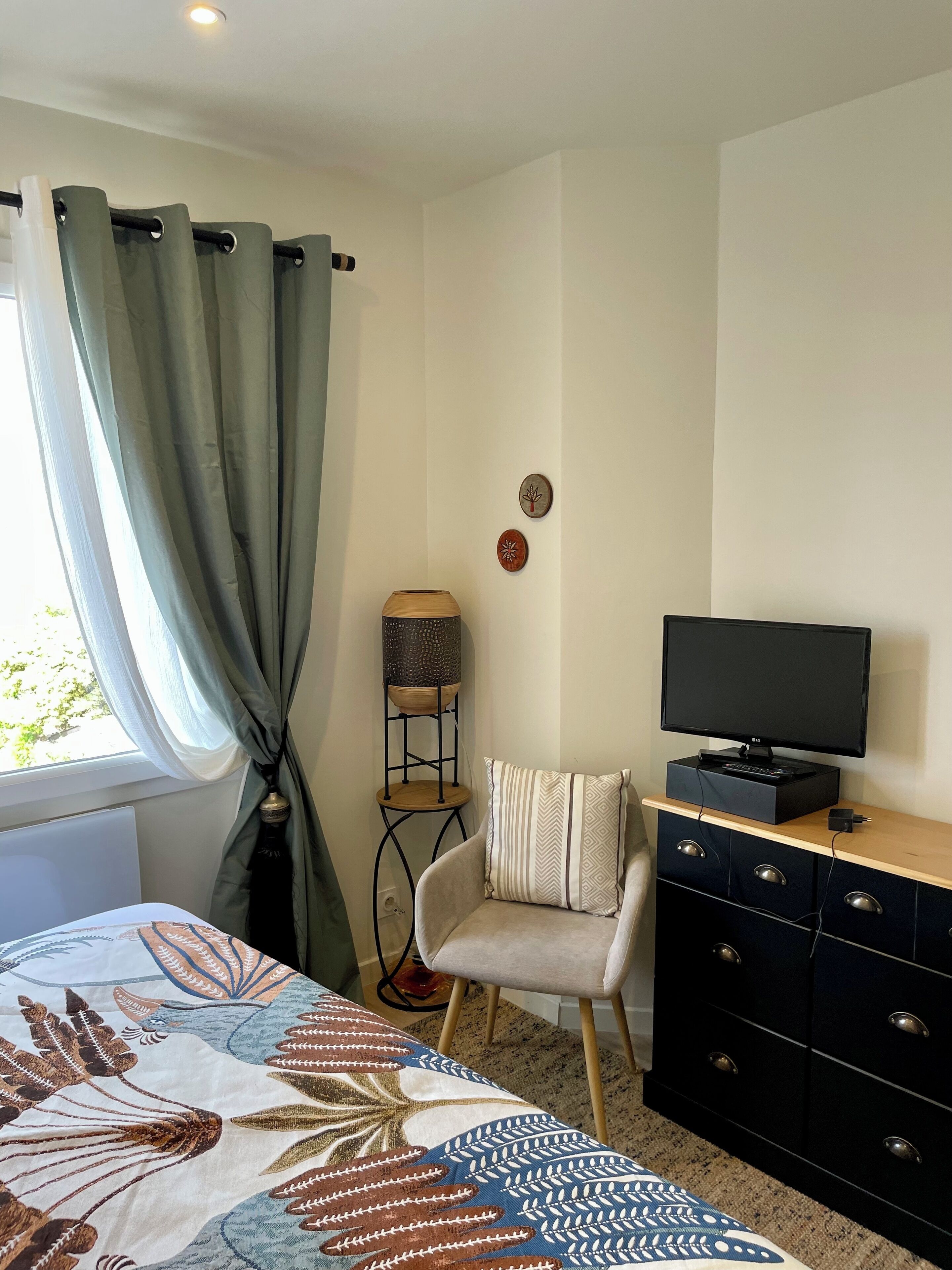 Ein Schlafzimmer mit einem Bett, einem Fernseher auf einer Kommode, einem Sessel und einer Lampe.