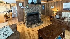 A cozy cabin interior with a stone fireplace, wooden walls, a television, and a dining area. - Snowshoe Luxury Ski Lodge @ TopShelfStays (Slatyfork)