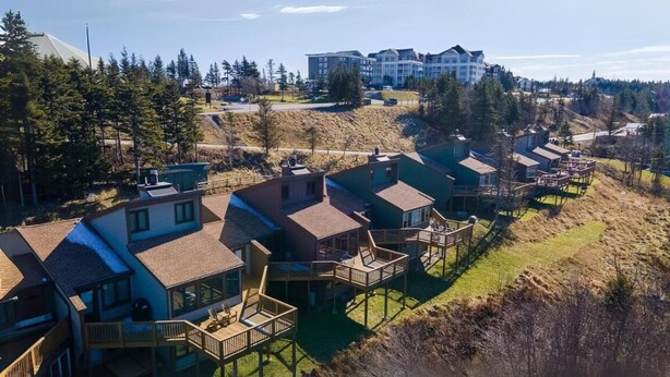 A residential area with houses featuring wooden decks and a view of a hill with buildings in the background. - Snowshoe Luxury Ski Lodge @ TopShelfStays (Slatyfork)