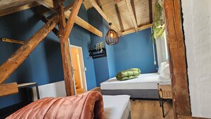 A rustic room with exposed wooden beams, a bed with a green pillow, a white mattress, and a brown blanket. - Alte Schreinerei, Modernisiert Fachwerkhaus mit Fernblick auf die Berge 12-16 P (Diemelsee)