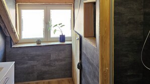 A room with a sloped ceiling, a window with a view, a door, and a small plant on the windowsill. - Alte Schreinerei, Modernisiert Fachwerkhaus mit Fernblick auf die Berge 12-16 P (Diemelsee)