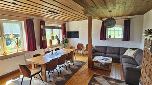 A cozy living room with a wooden ceiling, a sofa, a dining table with chairs, and a TV mounted on the wall. - Alte Schreinerei, Modernisiert Fachwerkhaus mit Fernblick auf die Berge 12-16 P (Diemelsee)