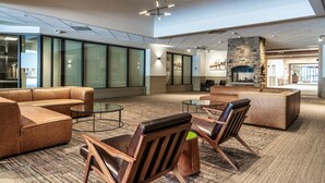 Un hall d’entrée spacieux, doté de canapés en cuir, de fauteuils en bois, d’une cheminée en pierre et de grandes fenêtres.