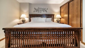 Une chambre à coucher avec un lit en bois, deux lampes de chevet, un élément décoratif mural et une armoire.