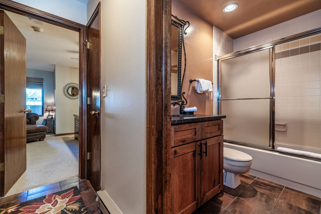 Un baño con tocador de madera, espejo, inodoro y zona de ducha.