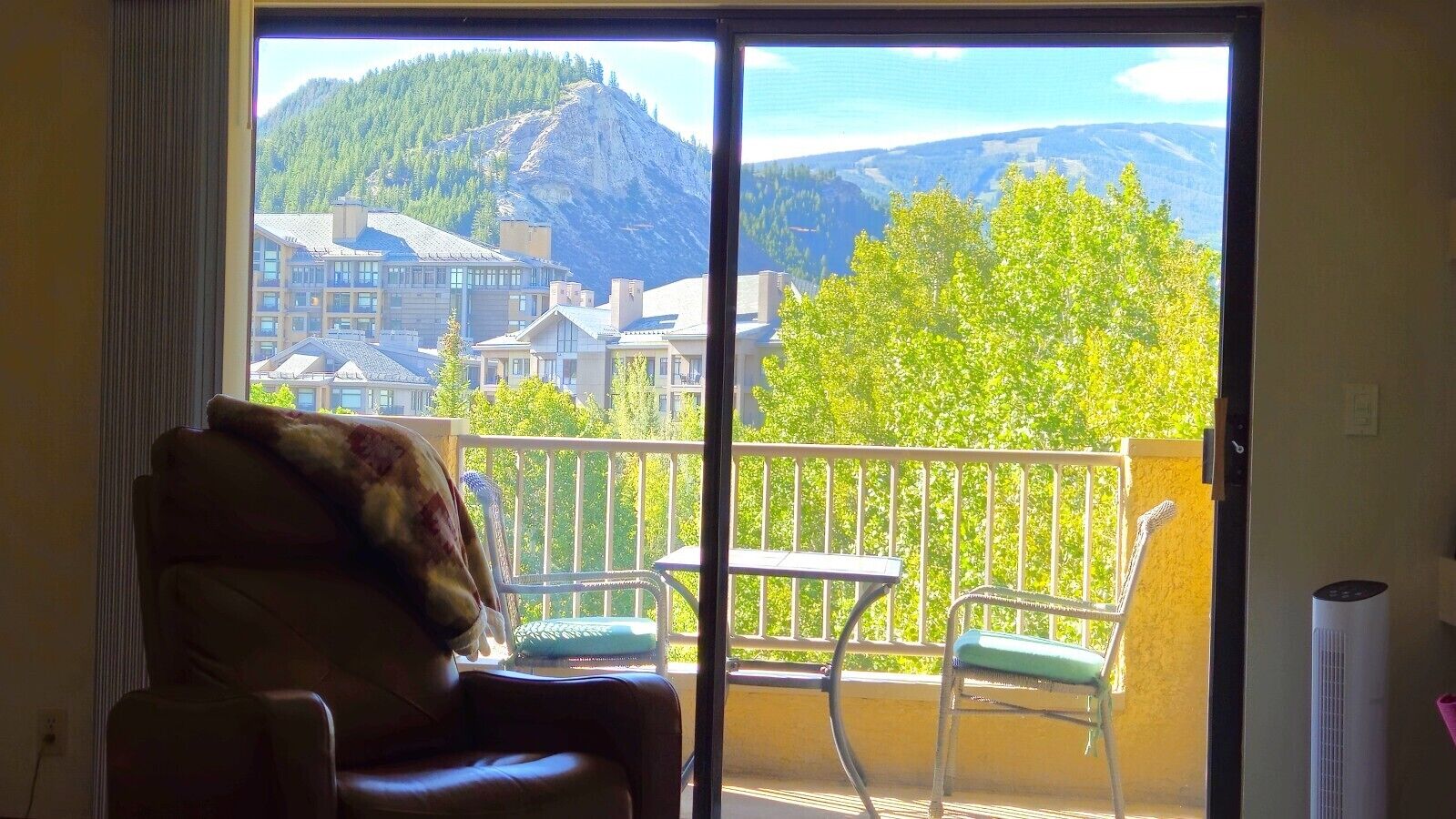 A room with a view of a mountain and a town through a sliding glass door.