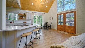Une cuisine moderne avec des poutres en bois, une grande fenêtre et un coin repas équipé de tabourets.