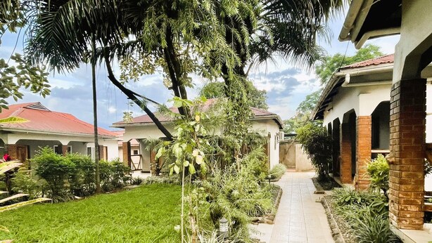 A residential area with a paved walkway, green lawns, and houses with red roofs. - Homefeeling Neneu Lodge (Moshi)