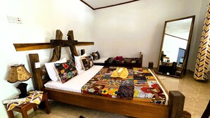 A bedroom with a wooden bed frame, a patterned bedspread, a bedside table with a lamp, and a mirror on the wall. - Homefeeling Neneu Lodge (Moshi)