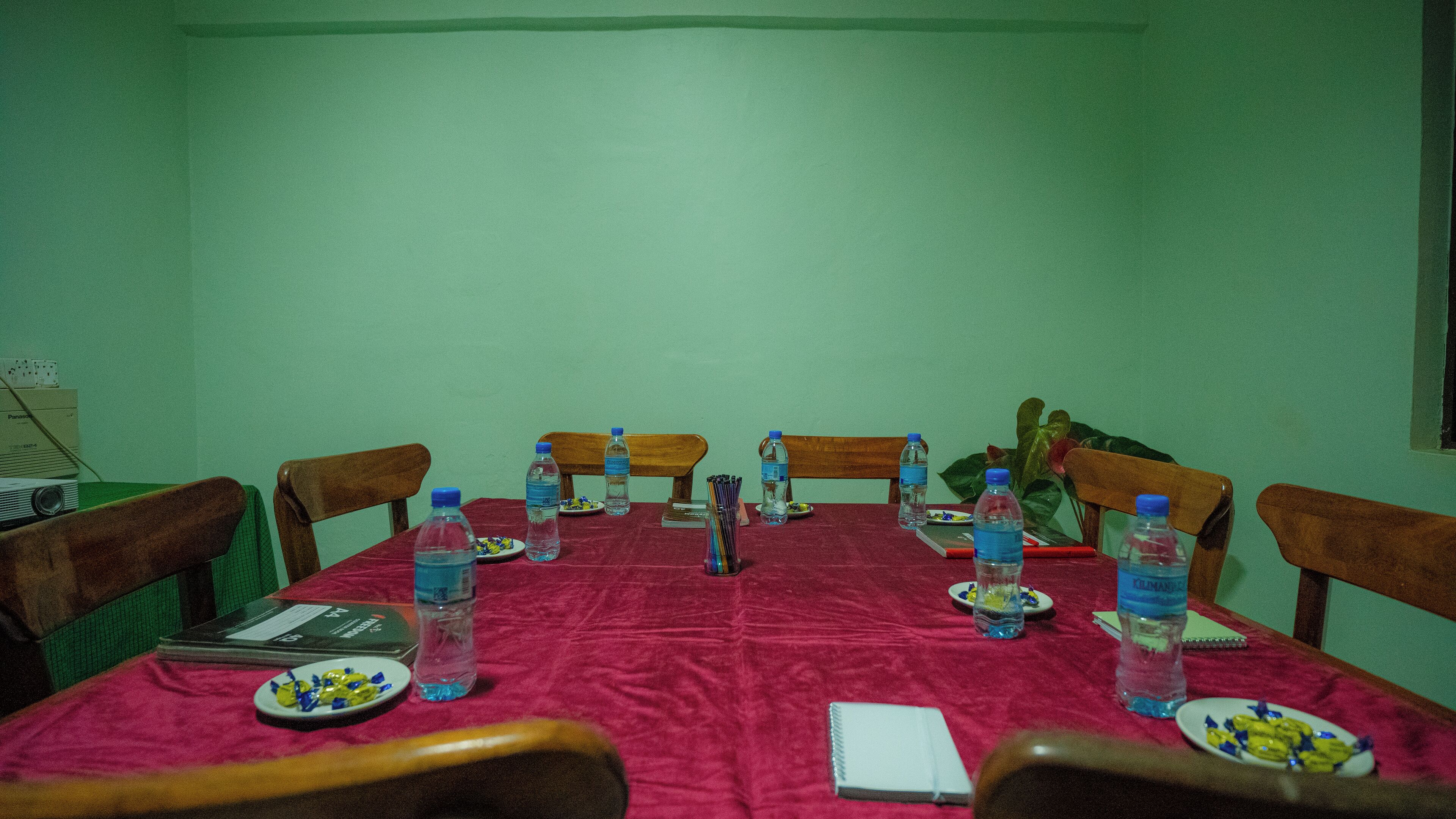 A conference room with a red tablecloth, wooden chairs, and water bottles.