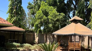 A house with a tiled roof, a small garden with various plants, and a wooden bench under a thatched structure. - Homefeeling Neneu Lodge (Moshi)