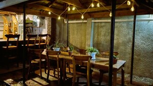 An outdoor dining area with wooden tables and chairs, string lights overhead, and potted plants on the table. - Homefeeling Neneu Lodge (Moshi)