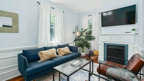 A living room with a blue sofa, a glass coffee table, a leather armchair, a fireplace, and a television. - Gorgeous Apt in Heart of Downtown: The Hall House (Wilmington)