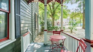 A covered porch with a table and chairs, a white picket fence, and a view of a street with trees and buildings. - Gorgeous Apt in Heart of Downtown: The Hall House (Wilmington)