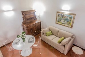 A living room with a beige sofa, a wooden cabinet, a dining table with chairs, and a framed picture on the wall.
