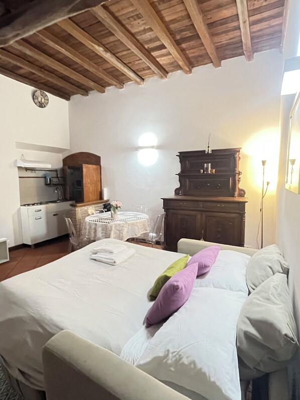 A bedroom with a bed, bedside tables, a dresser, a small table with chairs, and a kitchen area with a stove and sink.