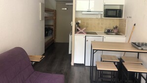 Une pièce compacte comprenant un coin cuisine, un canapé violet et une petite table à manger avec des chaises.