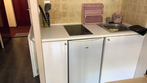 Une petite cuisine équipée comprenant un évier, un petit réfrigérateur et un plan de travail avec des ustensiles de cuisine.