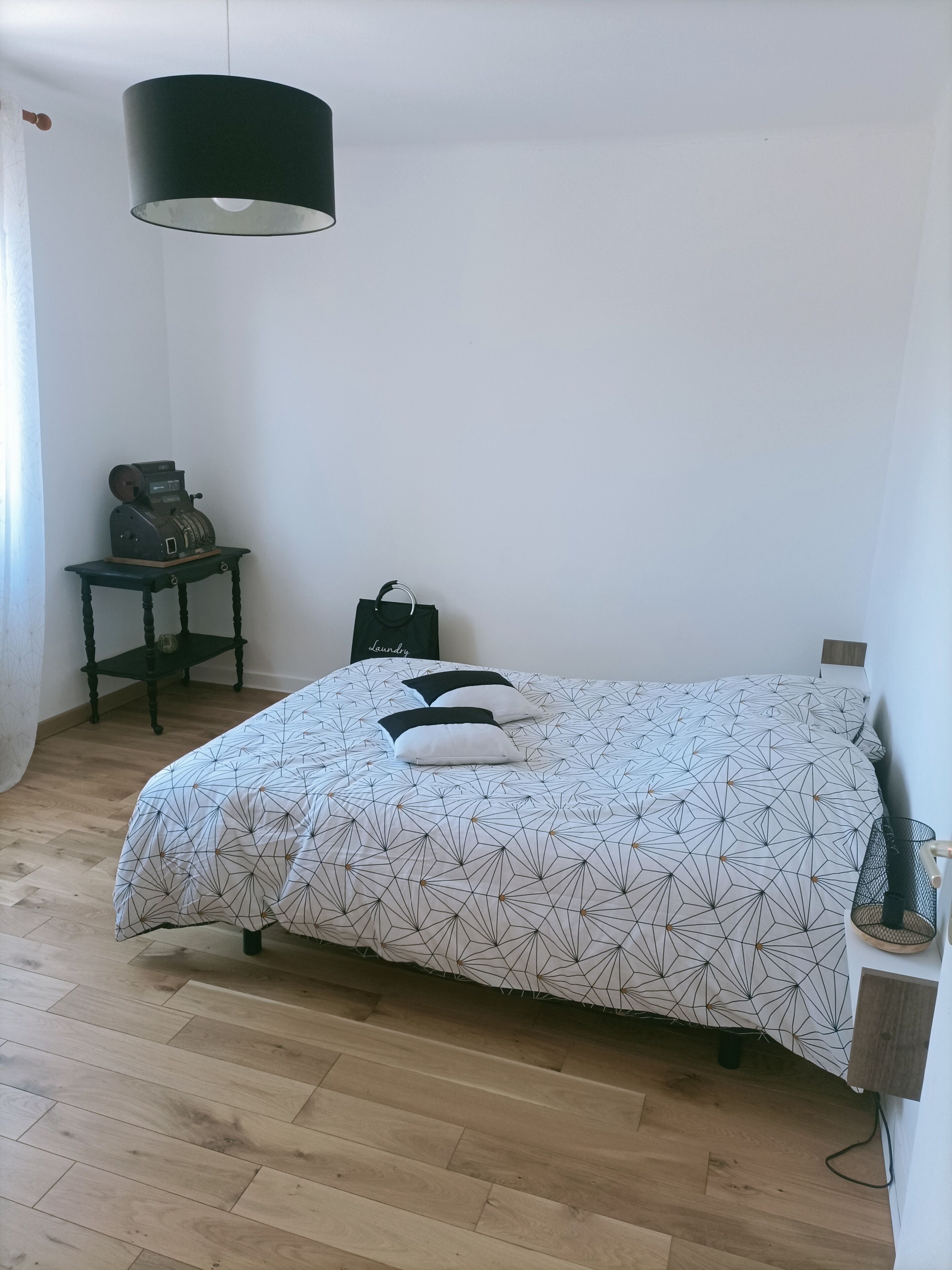 Une chambre à coucher avec un lit, une petite table sur laquelle se trouve une radio ancienne, une lampe suspendue et une étagère fixée au mur.