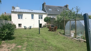 A residential property with a well-maintained lawn, a patio with outdoor furniture, a greenhouse, and a two-story house with a sloped roof. - Maison Avec Jardin Proche Centre Ville, 15 min de la Plage, 25 min de Brest (Lesneven)