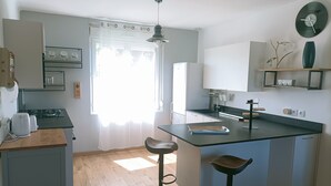 A modern kitchen with a central island, bar stools, a refrigerator, and a window with sheer curtains. - Maison Avec Jardin Proche Centre Ville, 15 min de la Plage, 25 min de Brest (Lesneven)