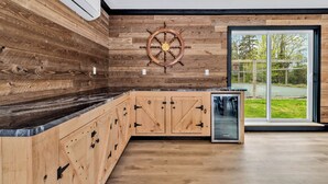 Une cuisine moderne avec des meubles en bois, un gouvernail de bateau et une grande porte-fenêtre coulissante donnant sur l’extérieur.