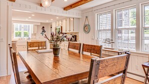 Une cuisine spacieuse avec une table à manger en bois, des meubles de rangement blancs et de grandes fenêtres.